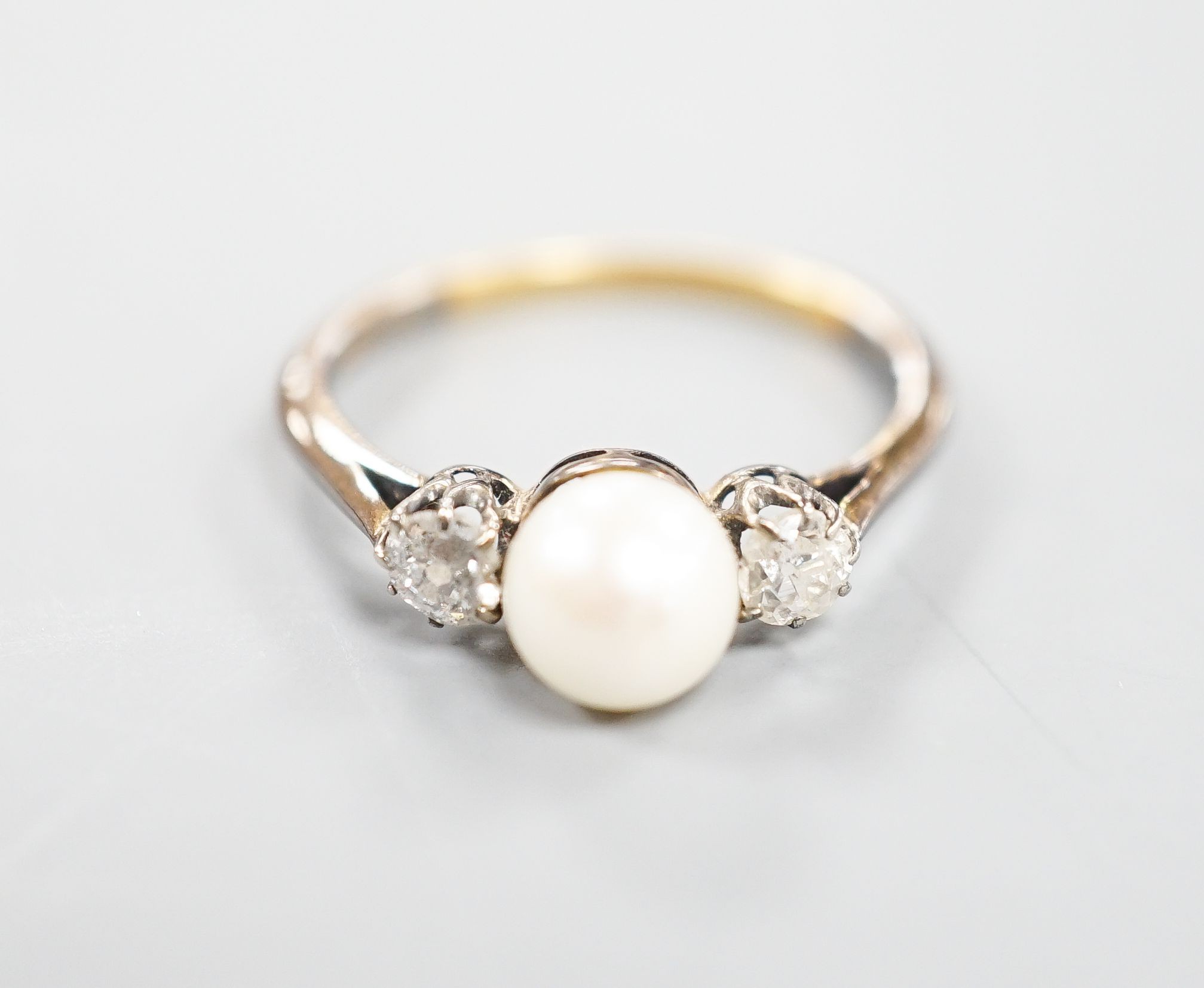An early 20th century 18ct, single cultured pearl and two stone diamond set ring, size N, gross weight 2.5 grams.